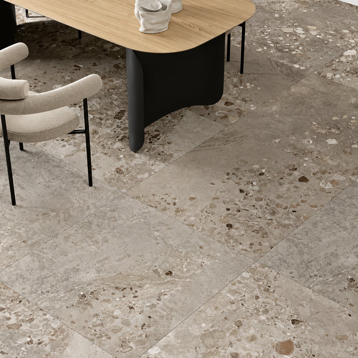 Un grand carrelage gris effet terrazzo recouvre le sol d'une salle à manger meublée d'une table en bois à pied noir et d'un fauteuil beige.