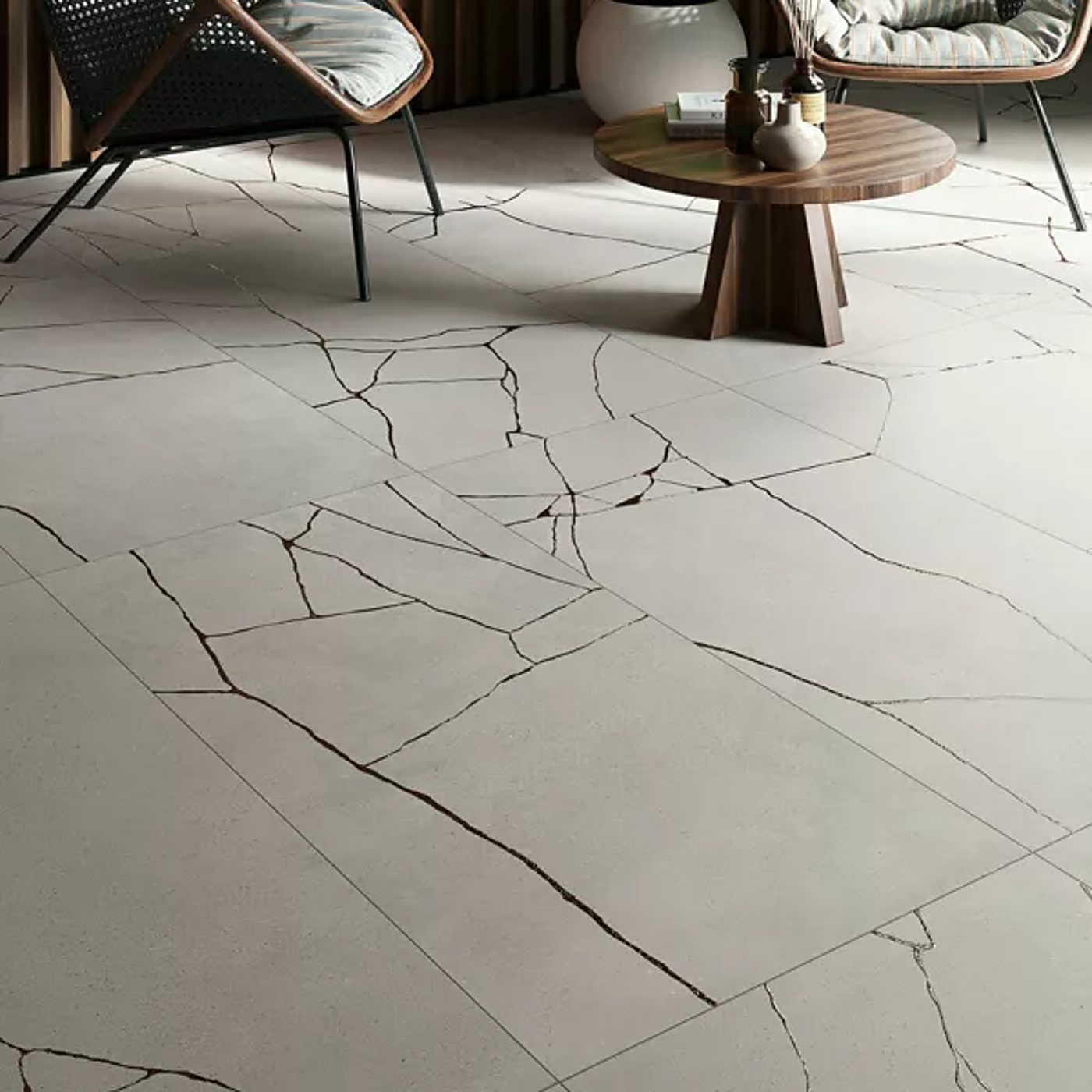 Sol en carrelage beige clair aux fines veines noires irrégulières, avec fauteuils en rotin et table basse en bois au fond.