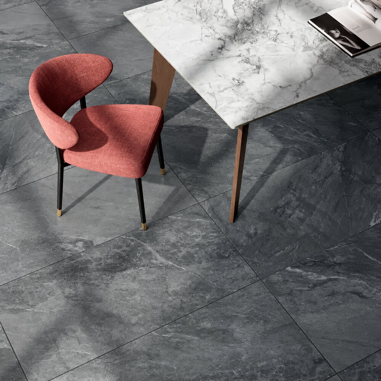 Vue de dessus d'un sol en grand carrelage gris anthracite effet pierre, avec une chaise en tissu rose et une table à plateau en marbre blanc.