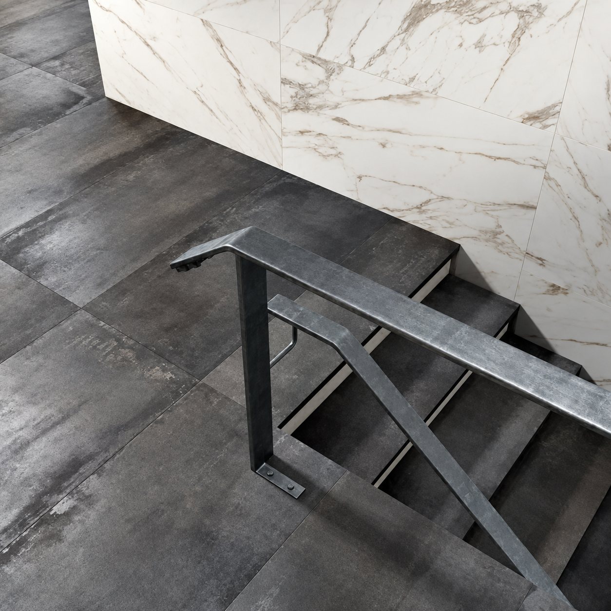 Un escalier recouvert de grands carreaux gris anthracite effet métal, avec une rampe en acier et un mur habillé de carreaux effet marbre blanc.
