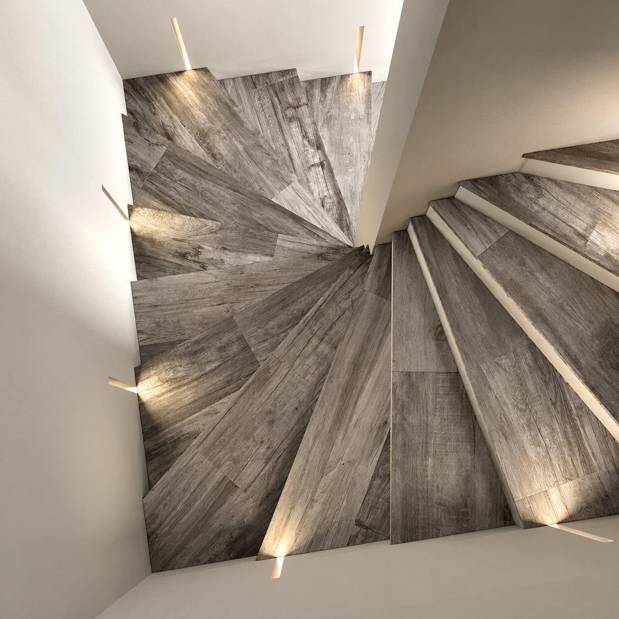 Vue de dessus d'un escalier tournant dont les marches sont recouvertes de carrelage gris effet bois et éclairées par de petites appliques encastrées dans les murs.