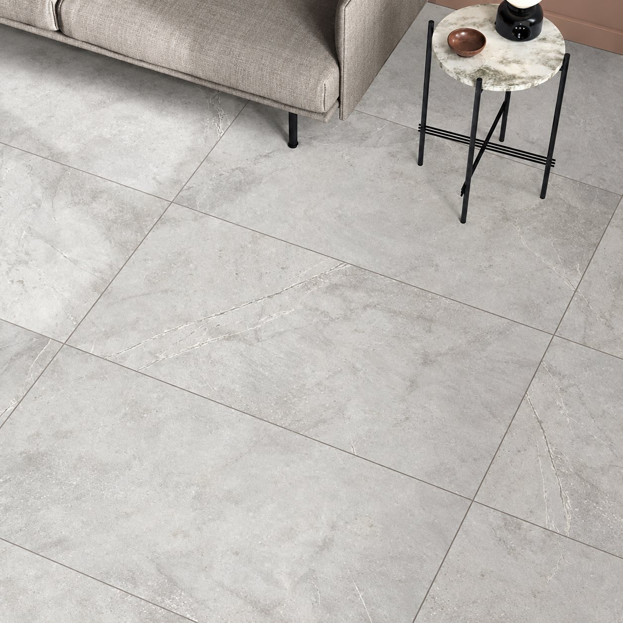 Sol en grands carreaux gris effet pierre dans un salon, avec un canapé beige et une petite table d'appoint en marbre aux pieds noirs.