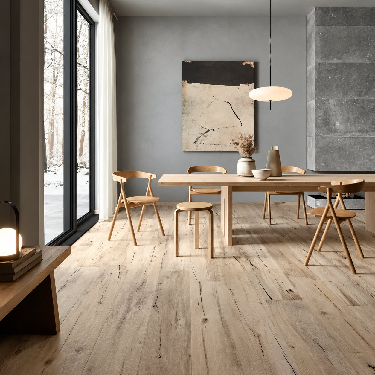 Salle à manger contemporaine aux murs gris avec une grande table en bois, des chaises en bois clair, une suspension blanche et un parquet clair vieilli.