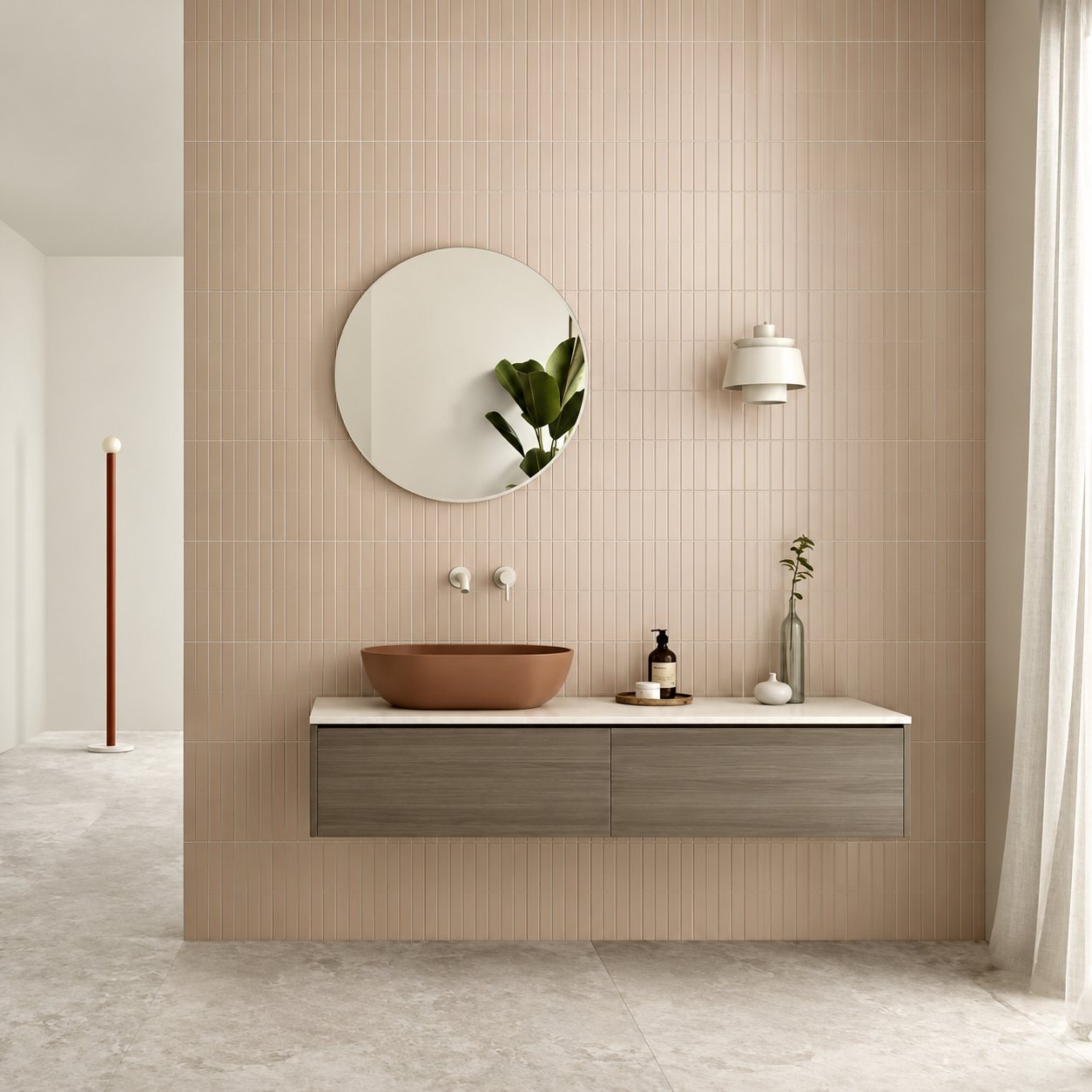 Salle de bain contemporaine aux murs carrelés rose pâle, avec un miroir rond, une vasque terracotta posée sur un meuble suspendu en bois et un sol en pierre claire.