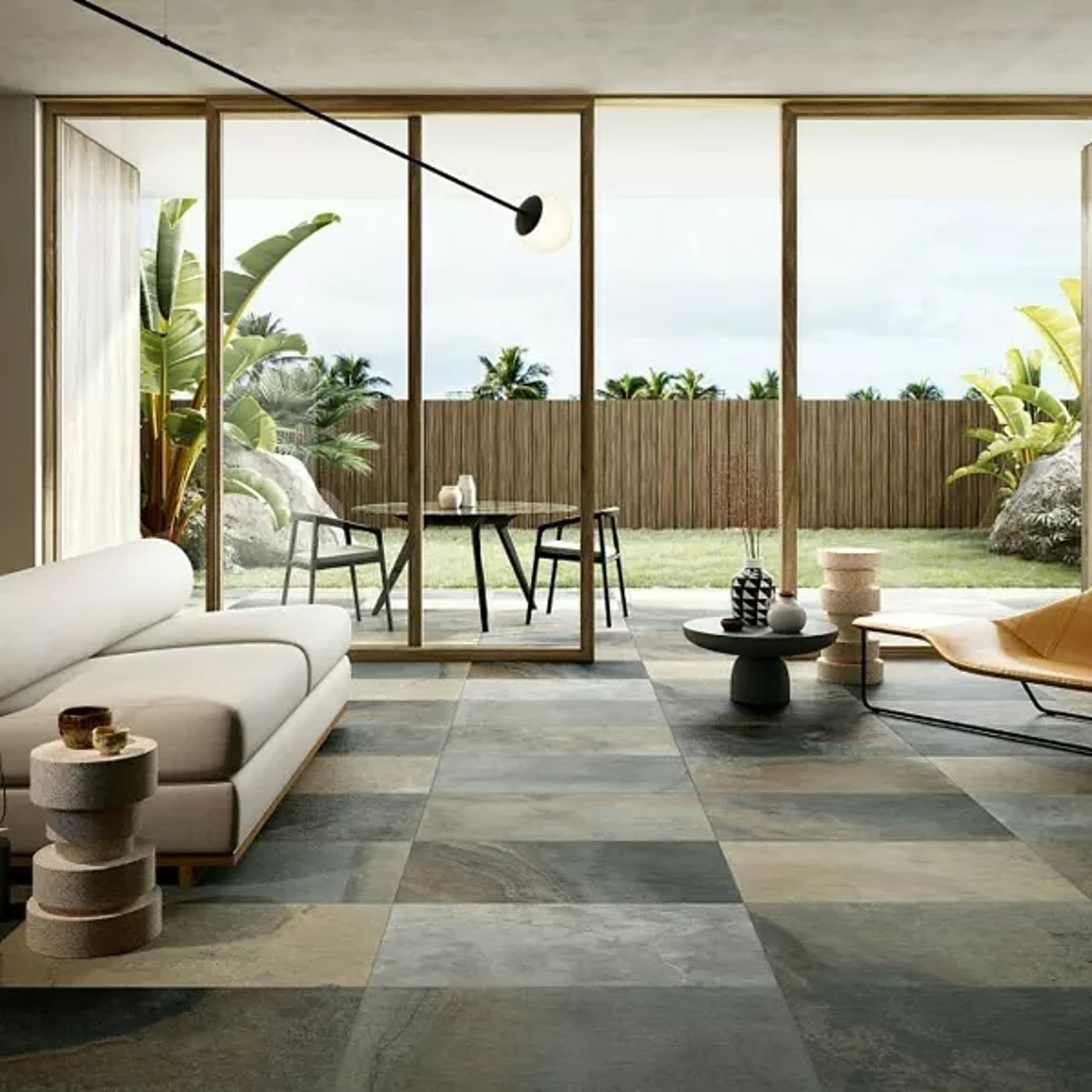 Un salon moderne avec canapé beige et sol en grands carreaux effet pierre nuancés de gris et d'ocre, ouvert par de larges baies vitrées sur un jardin tropical.