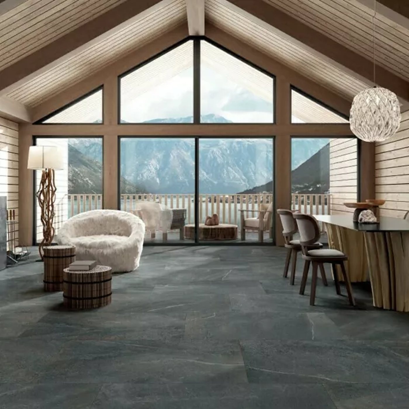 Salon spacieux de chalet en bois avec grandes baies vitrées donnant sur les montagnes, fauteuil en fausse fourrure blanche et sol en grands carreaux gris effet pierre.