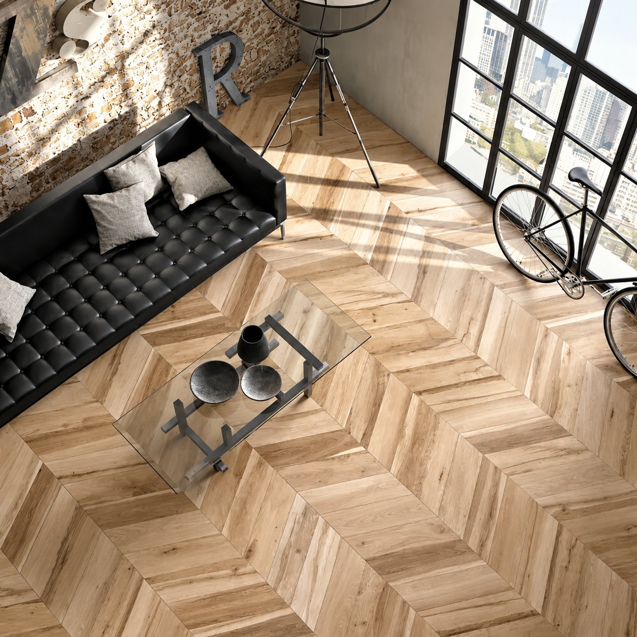 Vue du dessus d'un salon de style loft avec un canapé en cuir noir, une table basse et un vélo sur un sol en carrelage imitation parquet à chevrons.
