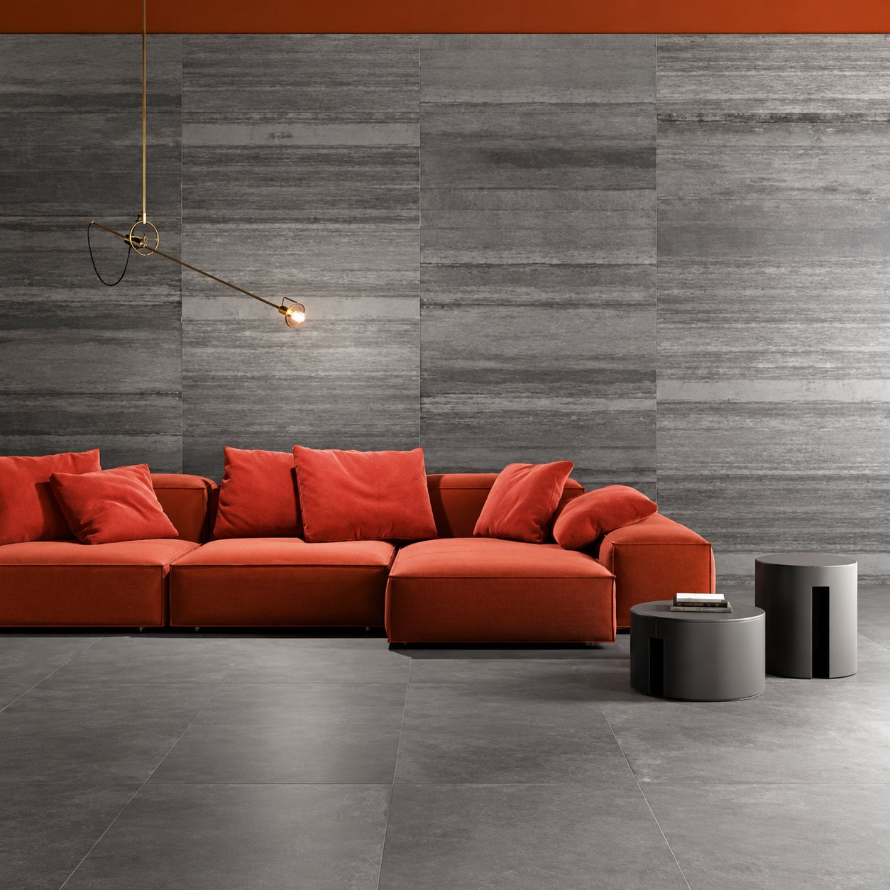 Un canapé d'angle orange avec coussins et deux tables basses noires dans un salon aux murs et au sol en grands carreaux gris.