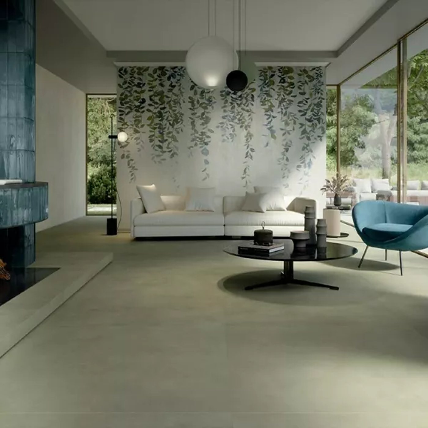 Un salon contemporain lumineux avec un canapé blanc devant un mur orné de feuillages, un fauteuil bleu, une table basse noire et un sol en grand carrelage vert-gris.