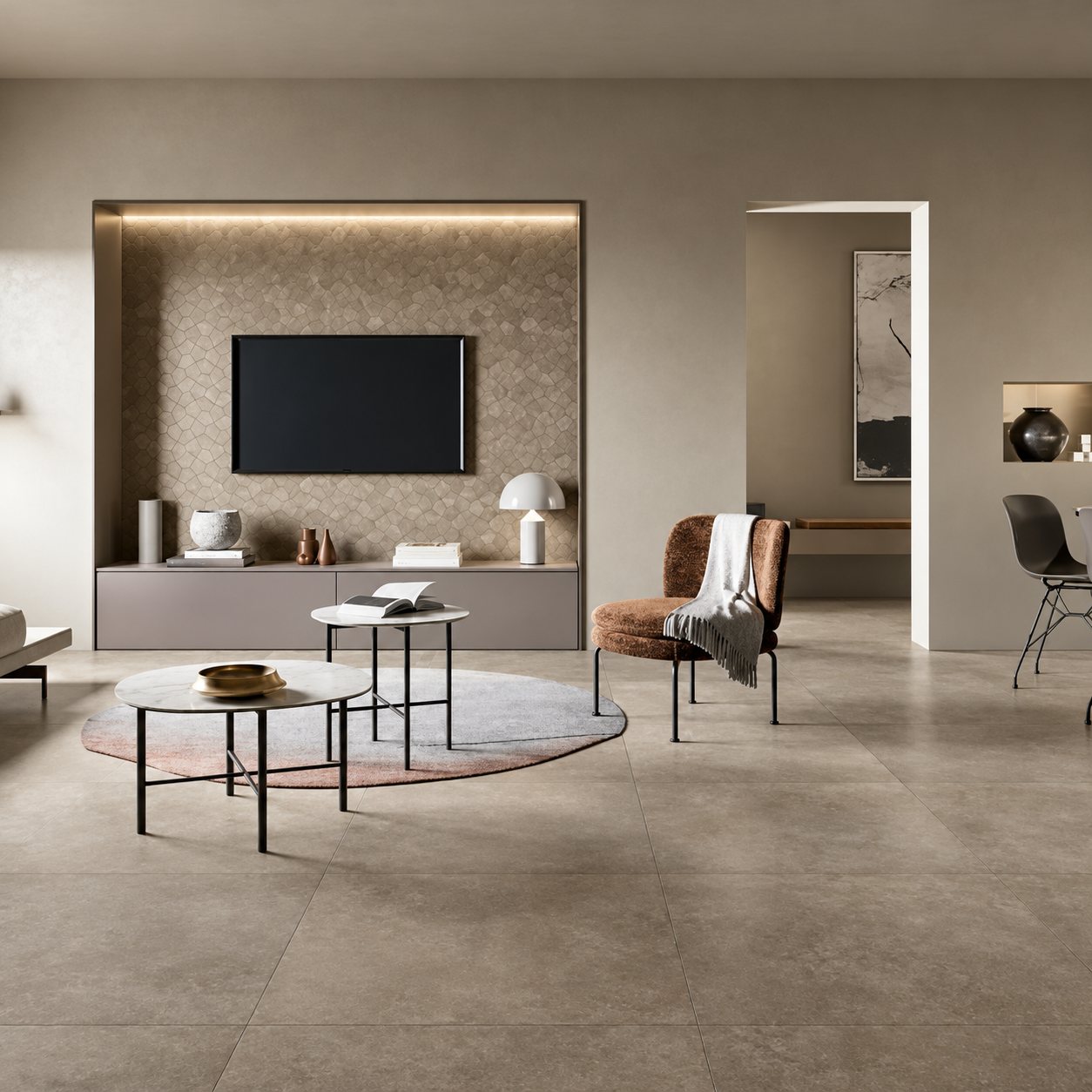 Salon contemporain aux teintes grises avec sol en grand carrelage, deux tables basses rondes, un fauteuil cuivré et un meuble télévision encastré dans une niche.